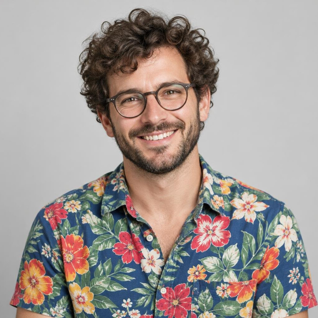 Smiling man with curly hair and round glasses in a floral shirt